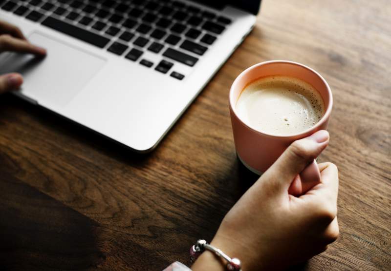 woman working on macbook holding coffee mug