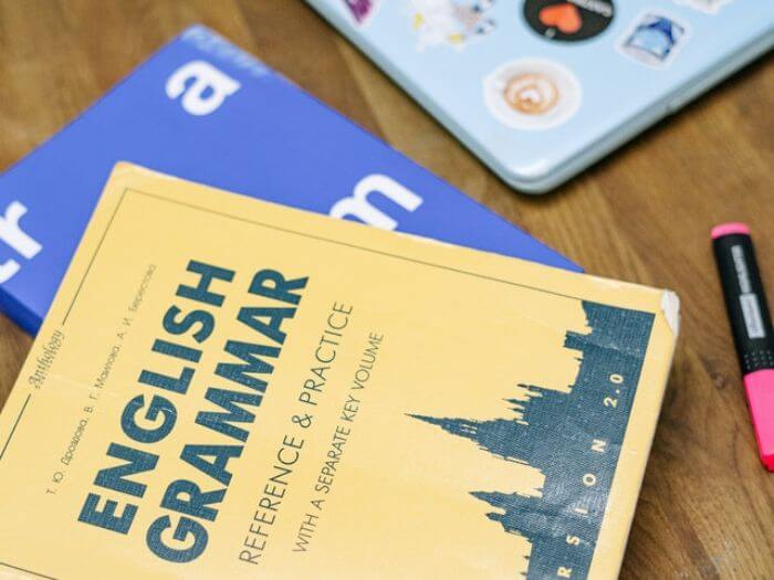 English grammar book on desk next to laptop