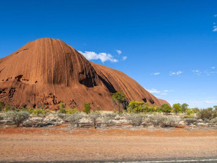 a large red rock formation in the desert with Uluru in the background, outback