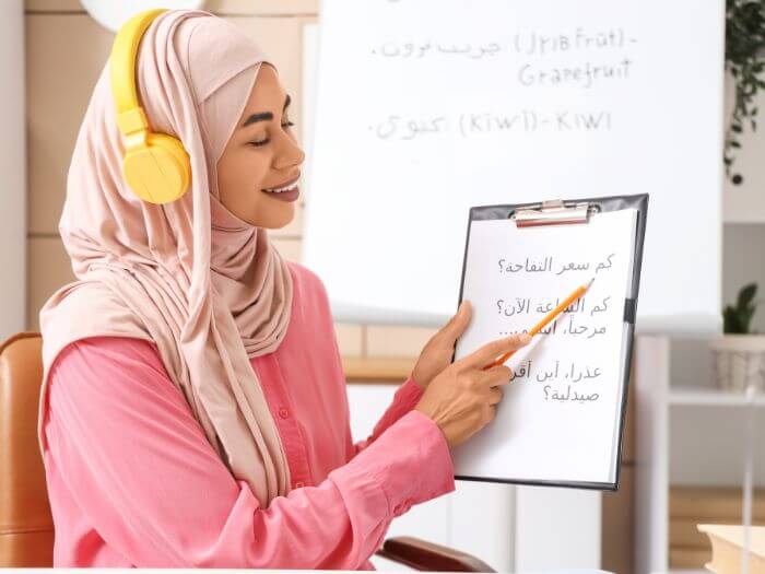 a woman wearing headphones pointing at a clipboard with Arabic script on it 