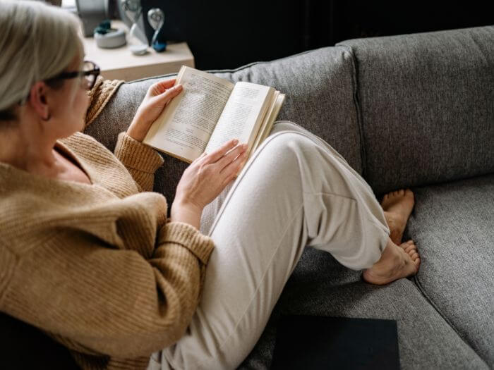 Woman in glasses with grey hair reading on couch